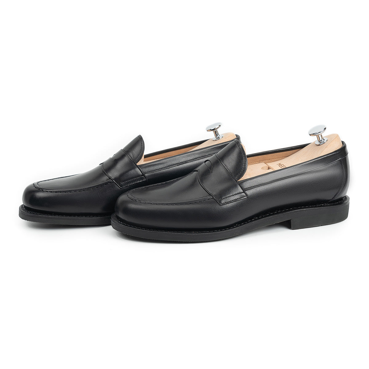 Meermin black calf penny loafers, side-by-side three-quarter view with shoe trees inserted, showing apron stitching and studded rubber sole